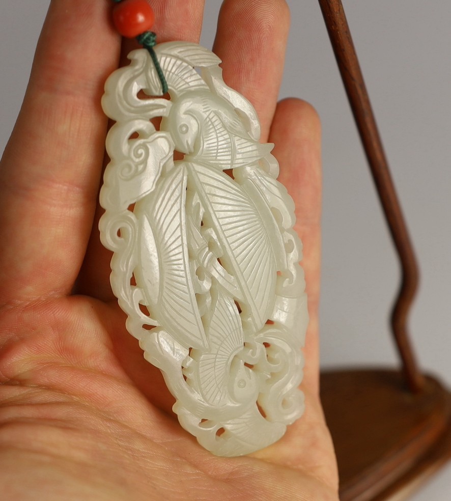 A Chinese white jade twin phoenix reticulated plaque, 19th century, 8.7cm, suspended from a wood stand with coral bead to the cord